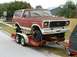 1979 Ford Bronco - A weathered red and white Ford Bronco is loaded onto a U-Haul trailer, ready for transport.