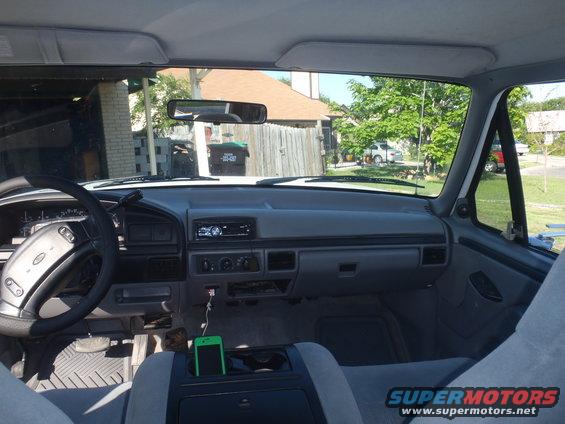 1997 Ford F-350 interior, gray dashboard, steering wheel, and seats. Green smartphone in center console