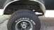 1993 Ford Bronco - Close-up of a vehicle's rear tire and wheel well shows rust and white trim.