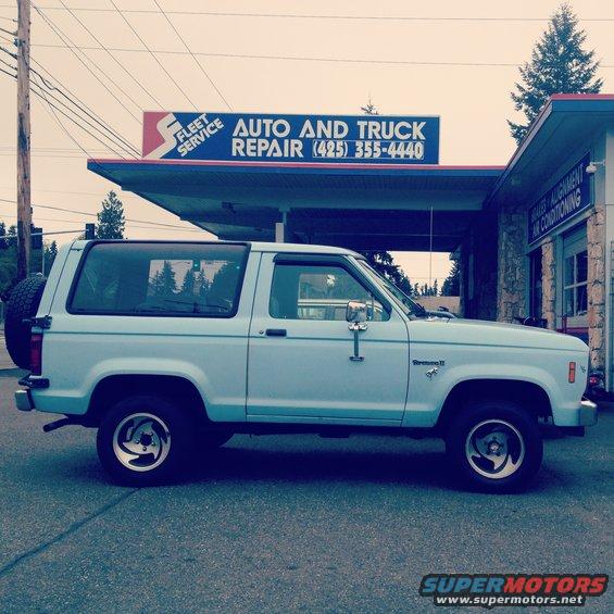 1985 Ford Bronco II parked on asphalt in front of an auto repair shop with a sign that says 'AUTO AND TRUCK REPAIR'