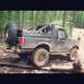 1995 Ford Bronco - A Ford Bronco navigates a muddy trail through a dense forest.
