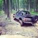 1995 Ford Bronco - A 1995 Ford Bronco tackles a challenging muddy path in a wooded area, with another vehicle visible in the distance.