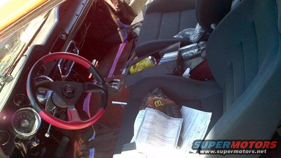 Interior shot of a vehicle with a two-tone steering wheel, papers on the passenger seat, and a can of soda