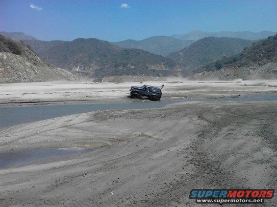 dark SUV navigating a muddy, watery terrain with mountains in the background