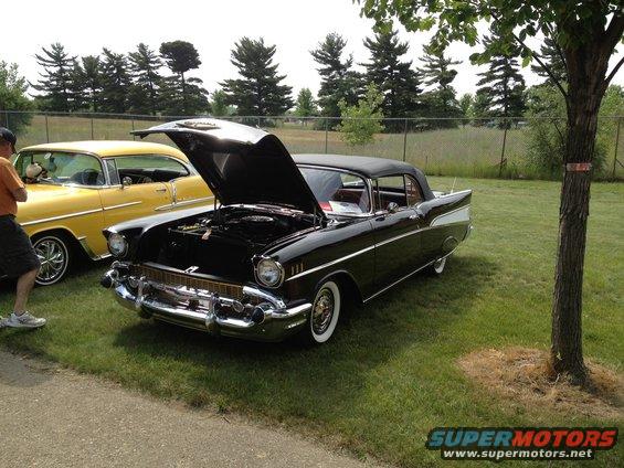 Black convertible with hood open next to a yellow coupe. Both cars are on grass