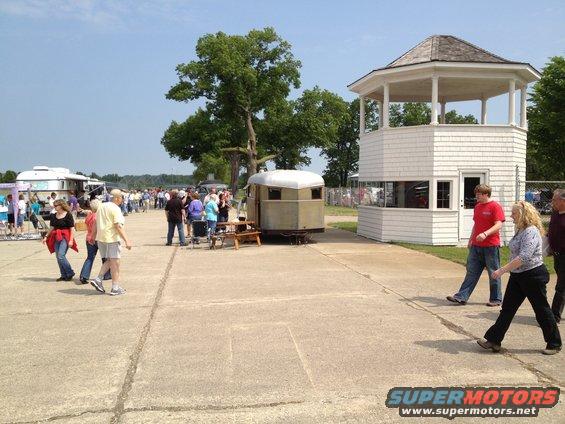 Outdoor event with people walking around trailers and a small building
