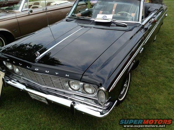 Black Plymouth convertible with chrome grille and trim, parked on grass next to a brown convertible