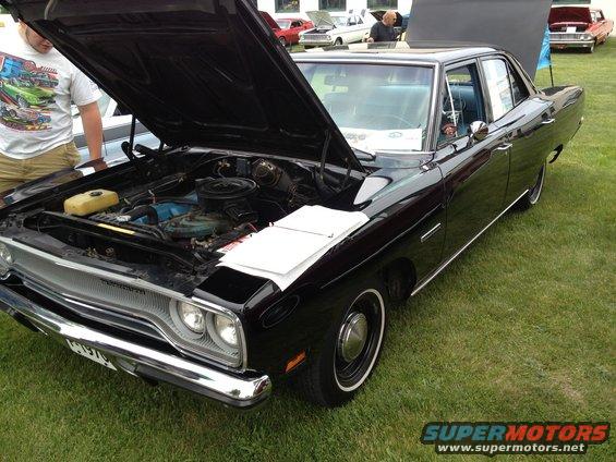 Black 1969 Plymouth GTX with hood open, showing engine. Other cars visible in background