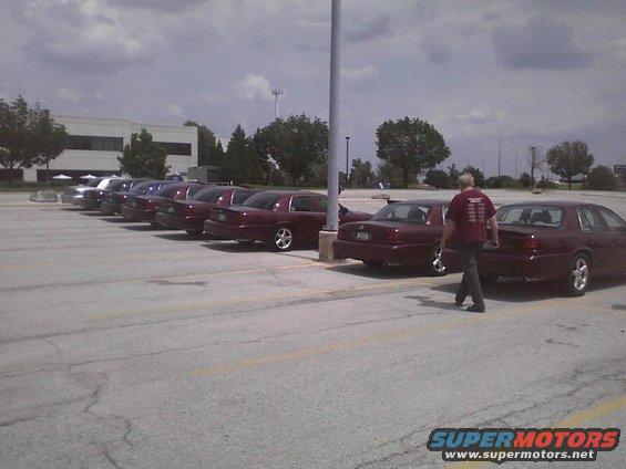 Several maroon 2003 Ford Crown Victorias parked in a lot with a man walking past