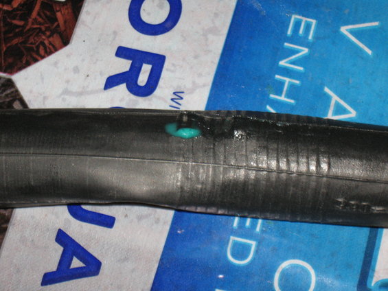 Bicycle inner tube with a turquoise sealant leak, showing ribbed texture and blue lettering on a white background