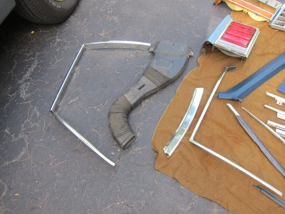 Car parts including a flexible duct, chrome trim, and a taillight assembly on a brown cloth