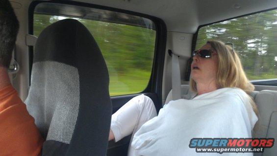 Woman sleeping in the back seat of a vehicle, with another passenger visible in the foreground