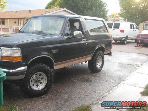 Black Ford Bronco with tan trim, parked outside next to a white van and a purple car