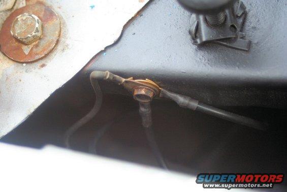 Close-up of a rusty bolt connecting wires on a vehicle's chassis