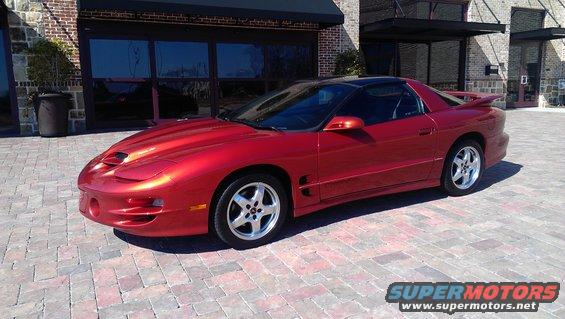 Red Pontiac Firebird parked on brick pavers in front of a building