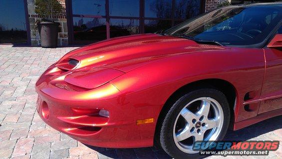 Red Pontiac Firebird parked on brick driveway, front quarter view