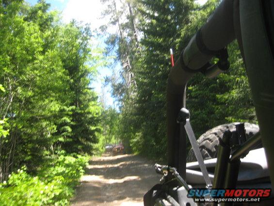 Off-road vehicles on a dirt road, trees on either side, tire and roll bar visible in foreground