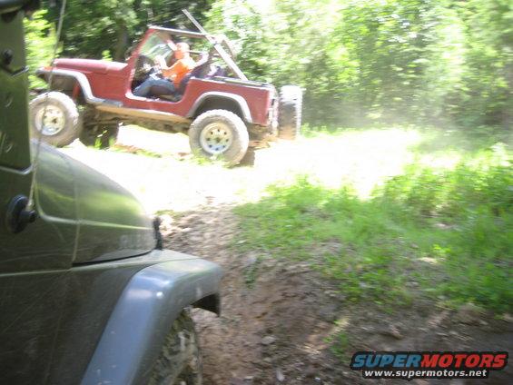 Two Jeeps driving on a dirt trail, one red and one dark green in the foreground