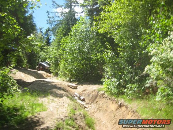 Off-road vehicle climbing a steep dirt trail surrounded by trees