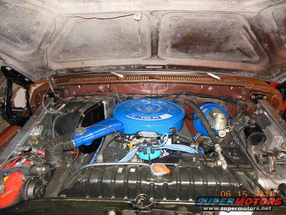 Engine bay with blue air cleaner and V8 engine components. Watermark reads 06 15 2018 SUPERMOTORS.NET