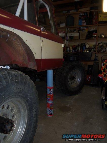 Red and white 1968 Ford Bronco side view, lifted with large tires, in a garage