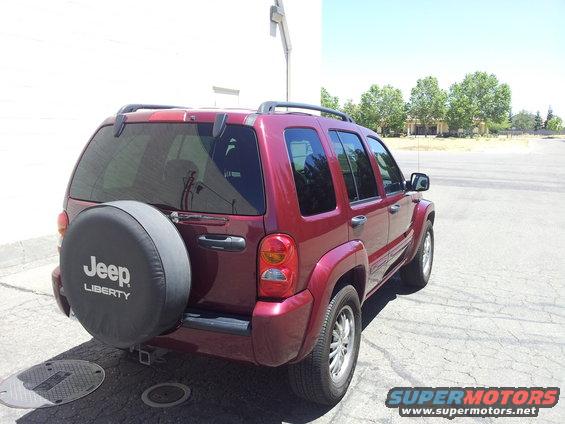 Red Jeep Liberty rear quarter view, spare tire cover with 'Jeep LIBERTY' text