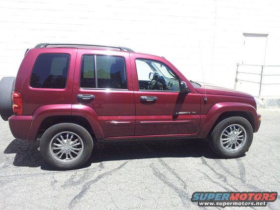 Red Jeep Liberty SUV side view with spare tire on rear