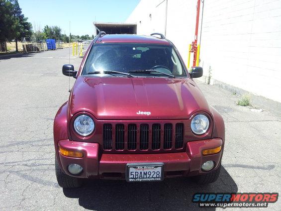 Red Jeep Liberty parked outside a building. Front view shows the grille, headlights, and license plate