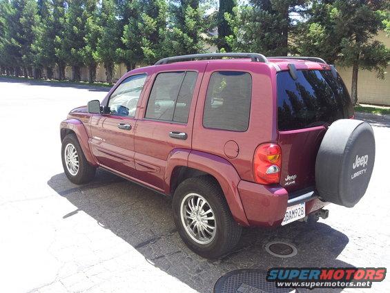 Red Jeep Liberty SUV parked on a street, rear quarter view. Spare tire cover reads 'Jeep Liberty'