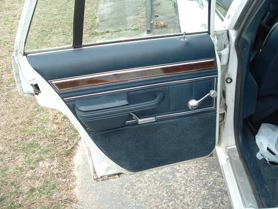 Interior of a car door showing blue upholstery, wood trim, and a manual window crank