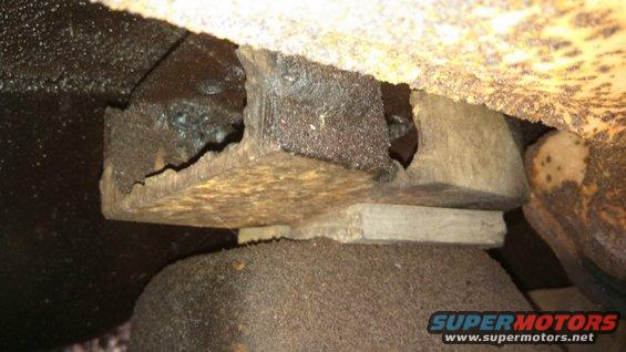 Rusted metal bracket with holes, resting on a dark, textured surface, with a lighter rectangular block underneath