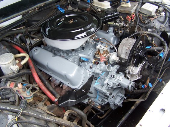 Engine bay showing a V8 engine with grey painted valve covers and black air cleaner. Various hoses and electrical components are visible
