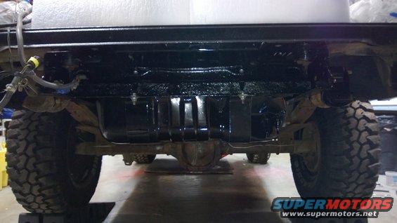 Undercarriage view of a vehicle with large tires and a black fuel tank