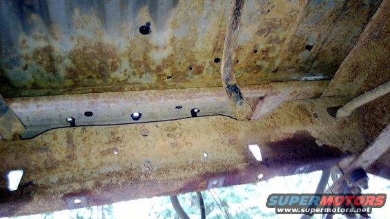 Heavily rusted undercarriage frame rails and crossmembers with visible holes and mounting points