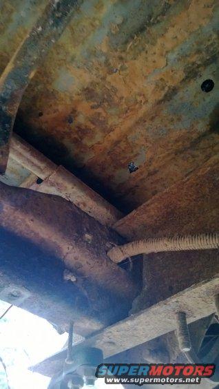 Undercarriage of a rusty vehicle, showing frame and exhaust components