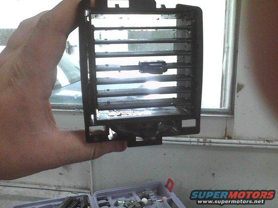 Hand holding a black car interior air vent with adjustable louvers