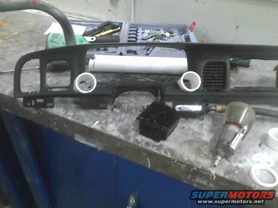 Car dashboard components on a workbench with tools, including an air-powered tool and a toolbox