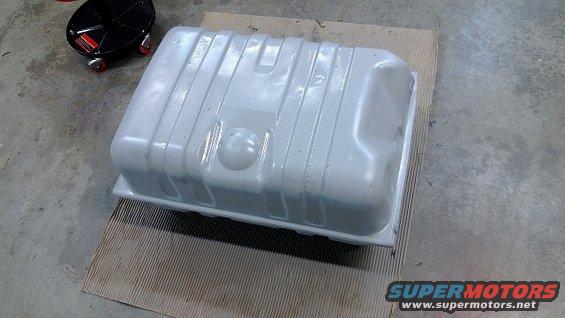 Gray fuel tank on cardboard with a black oil drain pan in the background