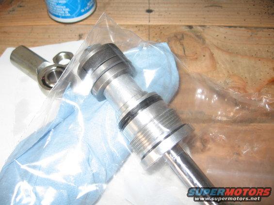 Steering linkage part in plastic bag on workbench. Supermotors.net logo visible