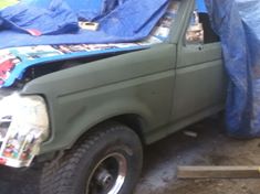 Ford Bronco covered in tarps, painted olive green primer. Front fender and headlight area are exposed