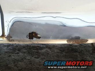Close-up of a corroded and patched vehicle rocker panel with a hole rusted through