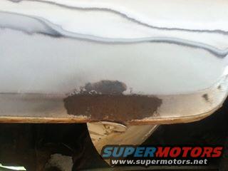 Close-up of a rusted lower body panel with SuperMotors logo