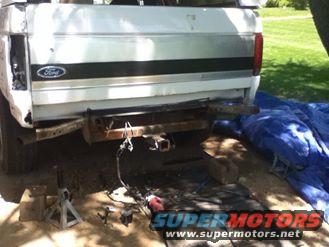 Rear of a white Ford pickup truck, possibly being worked on. Has a trailer hitch