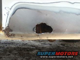 White metal panel with rust and a large hole, Supermotors.net logo visible