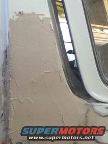 Close-up of body filler on a white vehicle's rear quarter panel