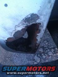 Close-up of a rusted-out panel on a vehicle, showing significant corrosion and damage