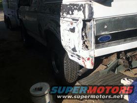 Damaged white vehicle rear quarter panel with missing taillight assembly. Another vehicle is partially visible to the left