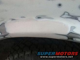 Close-up of a white vehicle's fender with body filler patches and a tire visible