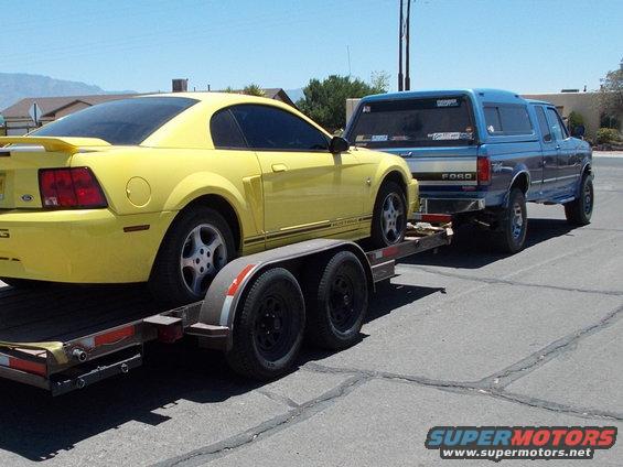 Yellow 2001 Ford Mustang on a trailer, towed by a blue Ford pickup truck