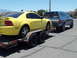 2001 Ford Mustang - A yellow 2001 Ford Mustang is transported on a trailer, pulled by a blue Ford pickup truck under a clear sky.